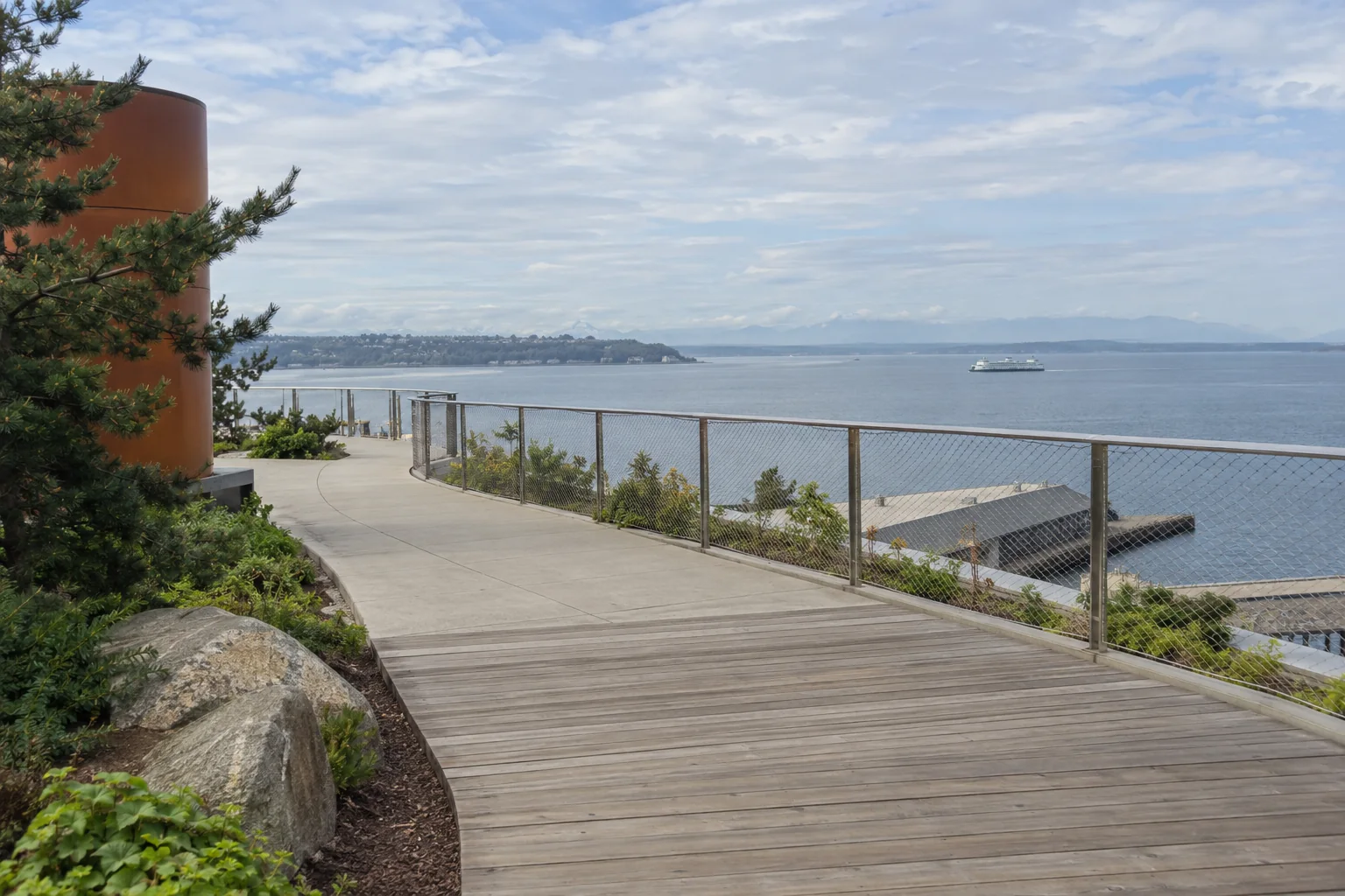 A timber-decked walkway with planted beds beside the railing high above the bay on the Seattle waterfront.
