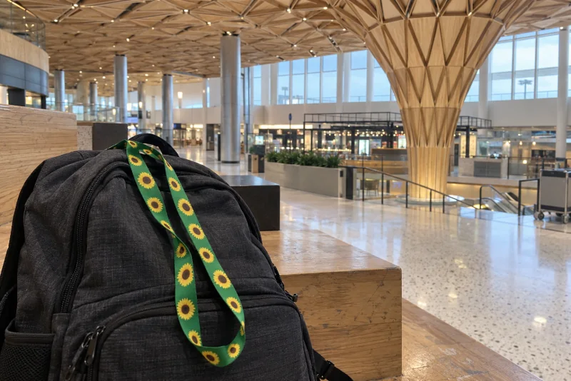A green sunflower lanyard on a dark backpack resting on the timber steps of the Central Terminal at Seattle-Tacoma airport.