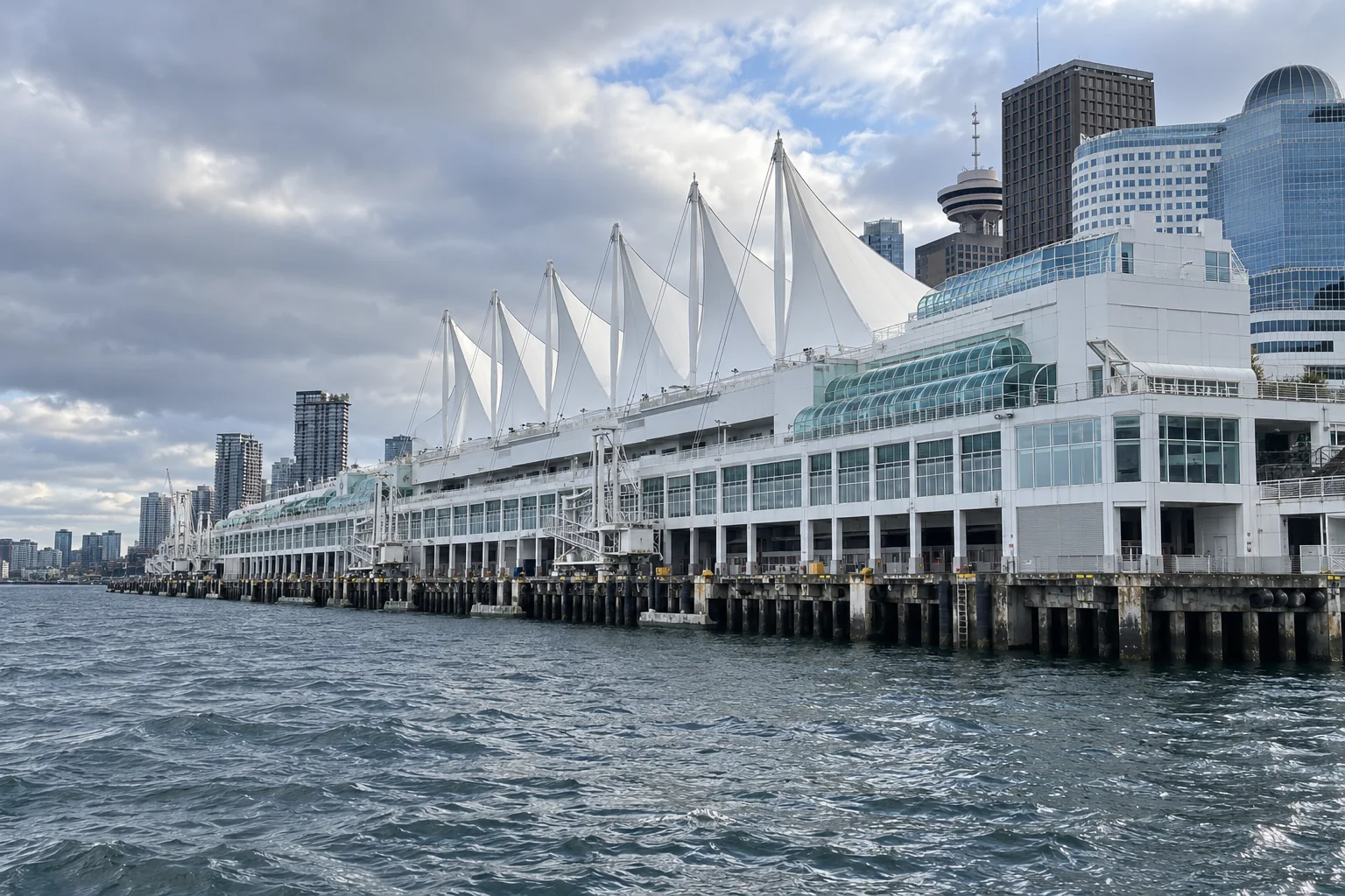 The white sail roofs of Canada Place in Vancouver seen from the harbour with office towers behind.