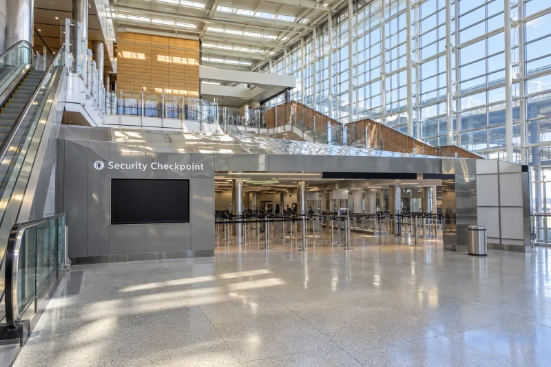 The bright checkpoint hall with escalators, a wood canopy and the glass wall.