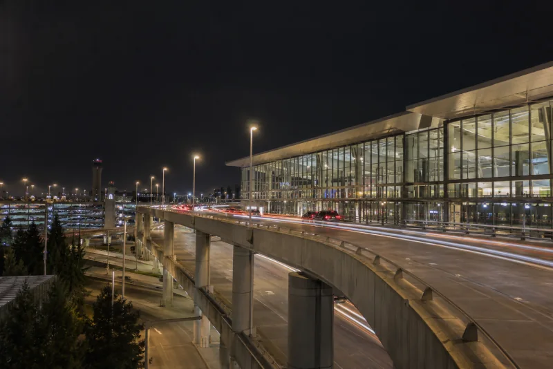 The Seattle-Tacoma airport terminal and elevated roadway at night with streaks of traffic light.