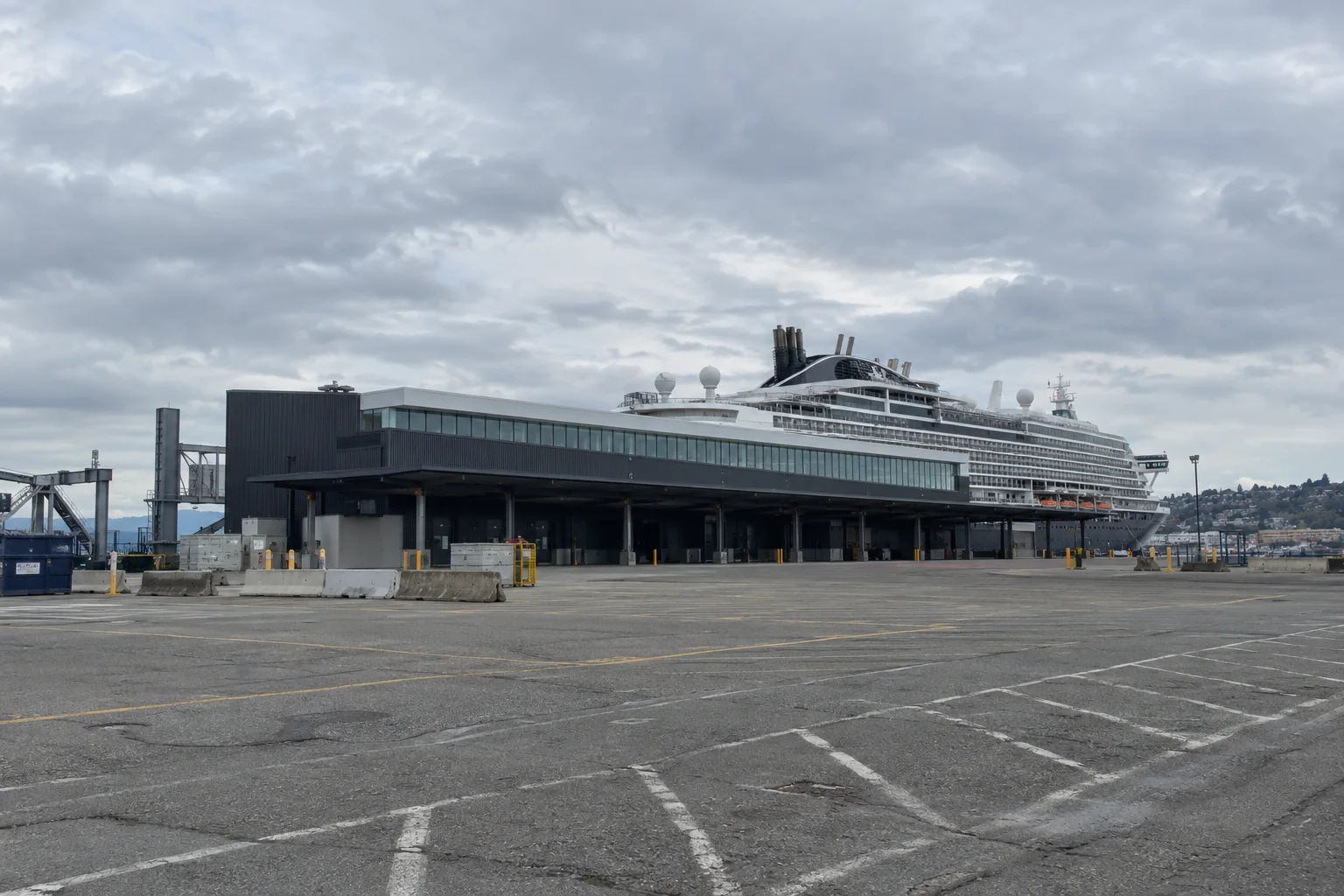 The low grey Pier 91 cruise terminal building in Seattle with a cruise ship behind it.