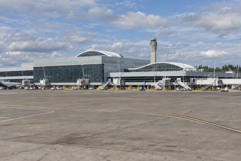 The glass-fronted North Satellite terminal at Seattle-Tacoma airport with its white arched roofs and control tower seen across the apron.