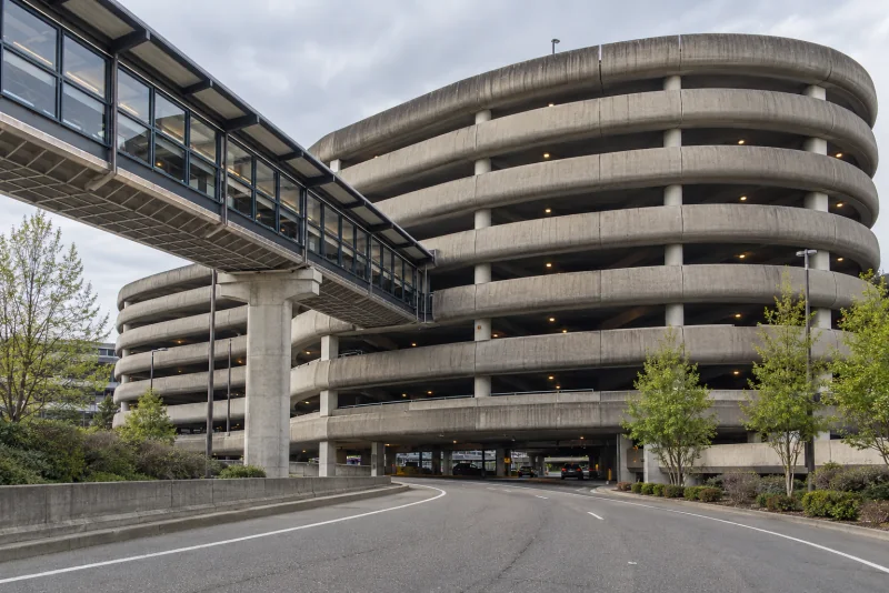 The curved concrete parking garage at Seattle-Tacoma airport with its ramp towers and the covered skybridge crossing the drive.