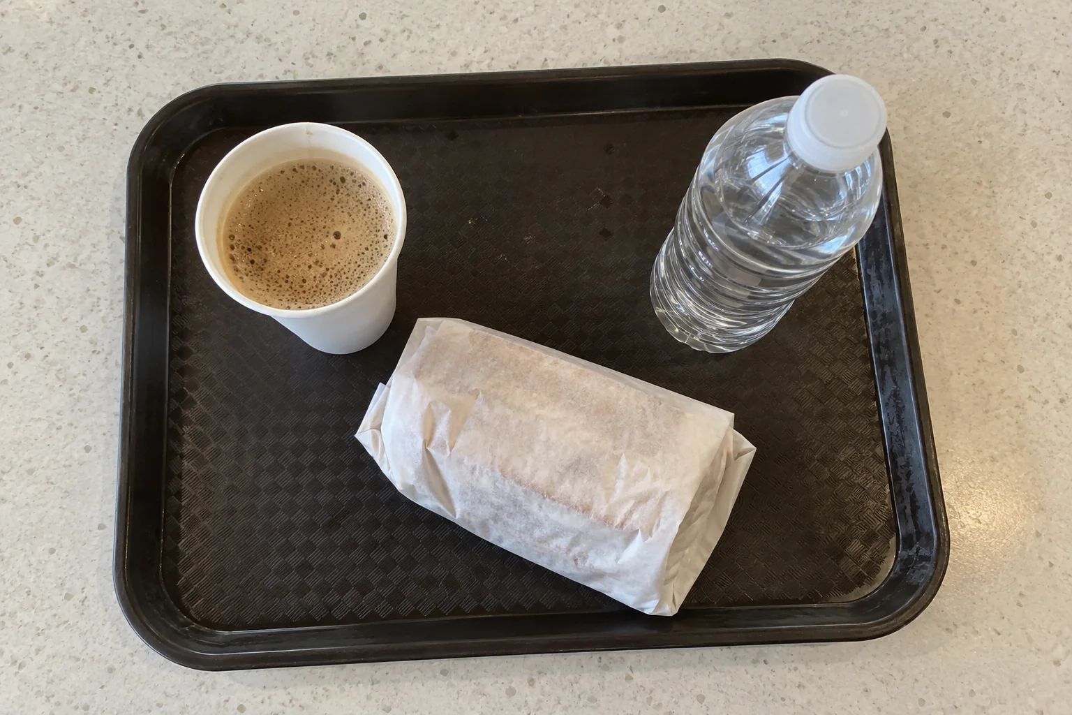 A tray with a wrapped sandwich, a paper cup of coffee and a bottle of water on a table at Seattle-Tacoma airport.