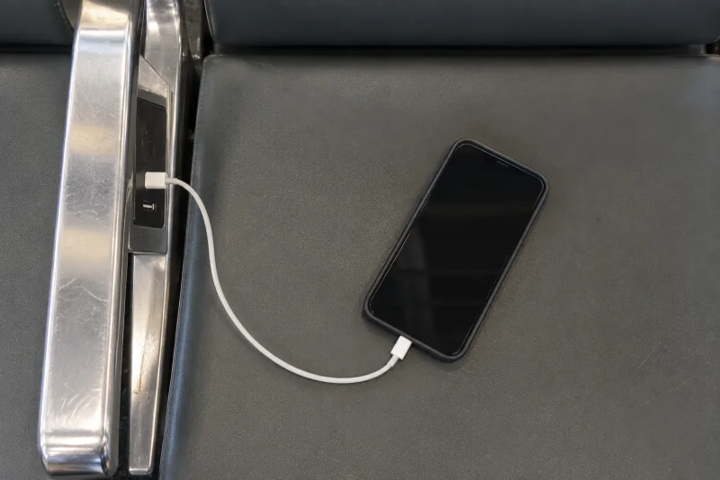 A phone charging from the power outlet on the armrest of a black gate seat at Seattle-Tacoma airport.