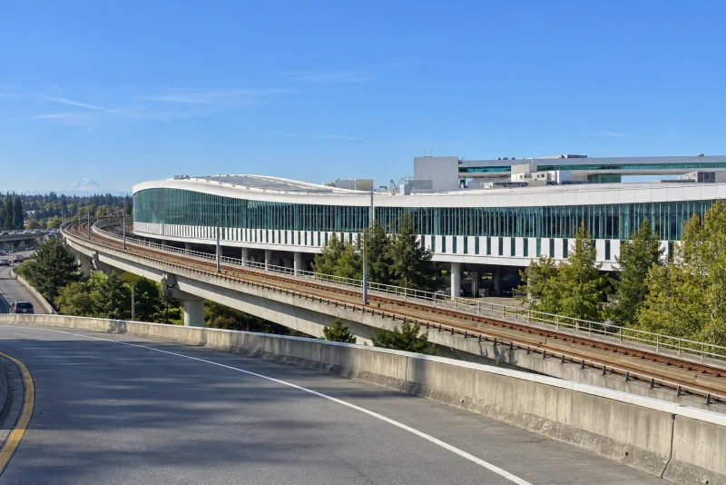 The long white International Arrivals Facility at Seattle-Tacoma airport seen from the roadway with its green glass band.
