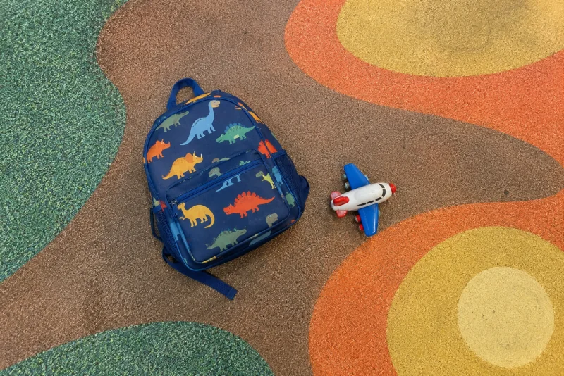 A child's dinosaur backpack and a toy airplane on the patterned floor of the play area at Seattle-Tacoma airport.