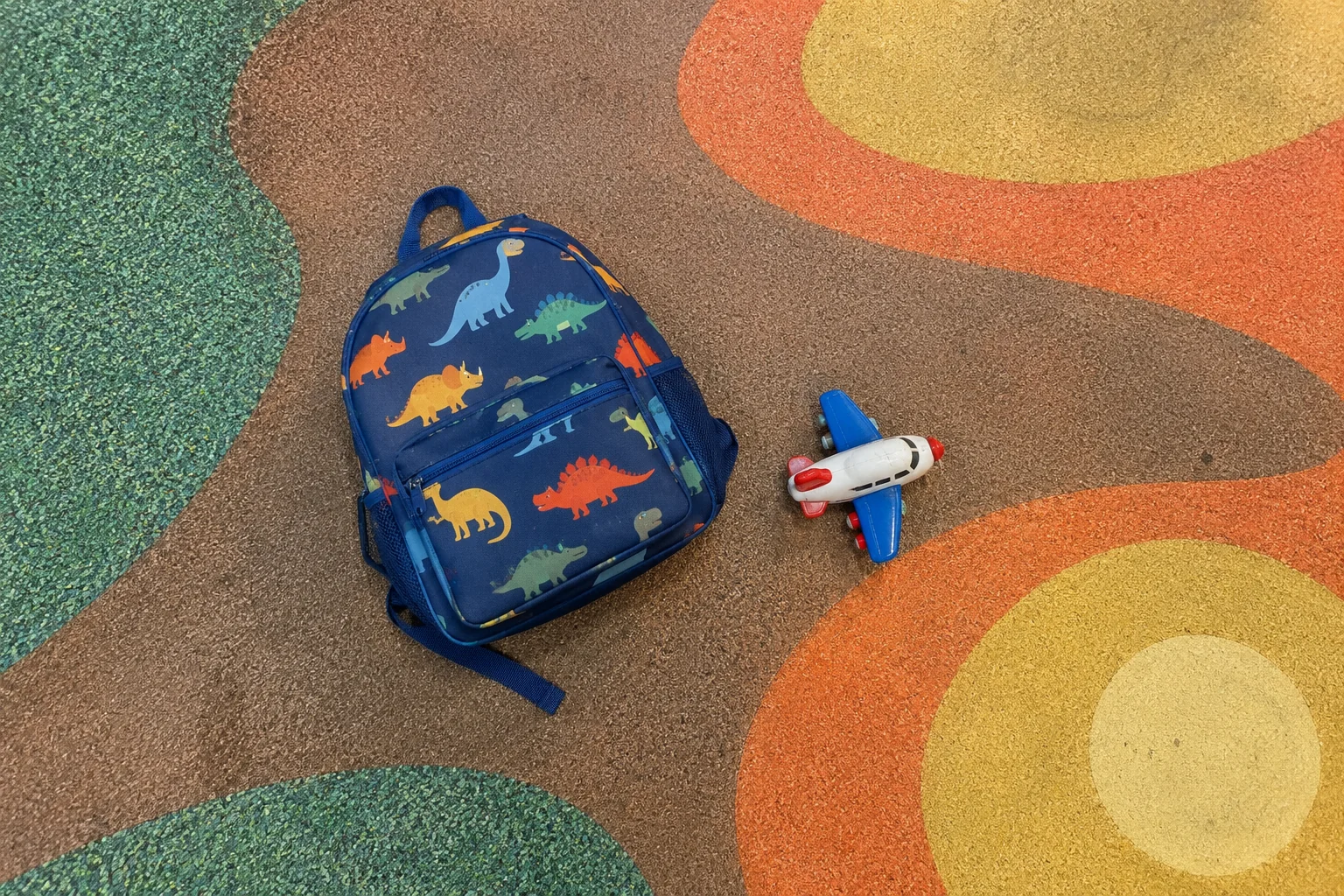 A child's dinosaur backpack and a toy airplane on the patterned floor of the play area at Seattle-Tacoma airport.