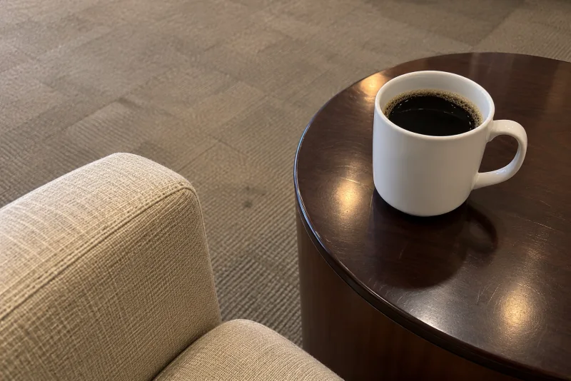 A cup of coffee on a small dark side table beside a cream armchair in a lounge at Seattle-Tacoma airport.