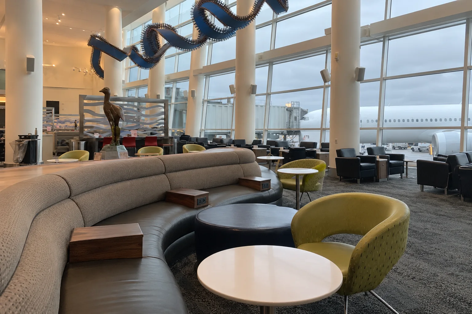 A long curved sofa and low tables in the Delta Sky Club hall at Seattle-Tacoma airport, with tall windows onto the apron.