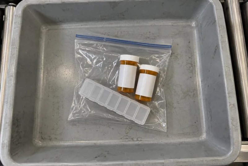 A clear bag with amber medicine bottles and a pill organizer in a grey screening bin at Seattle-Tacoma airport.