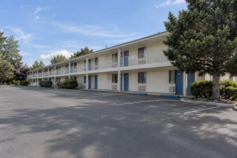 A long two-storey budget motel with cream siding and blue room doors beside a parking lot near Seattle-Tacoma airport.