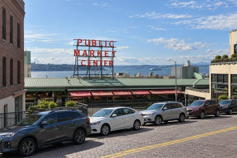 The market sign, green roof and red awnings of Pike Place Market from the street, with the harbour beyond.
