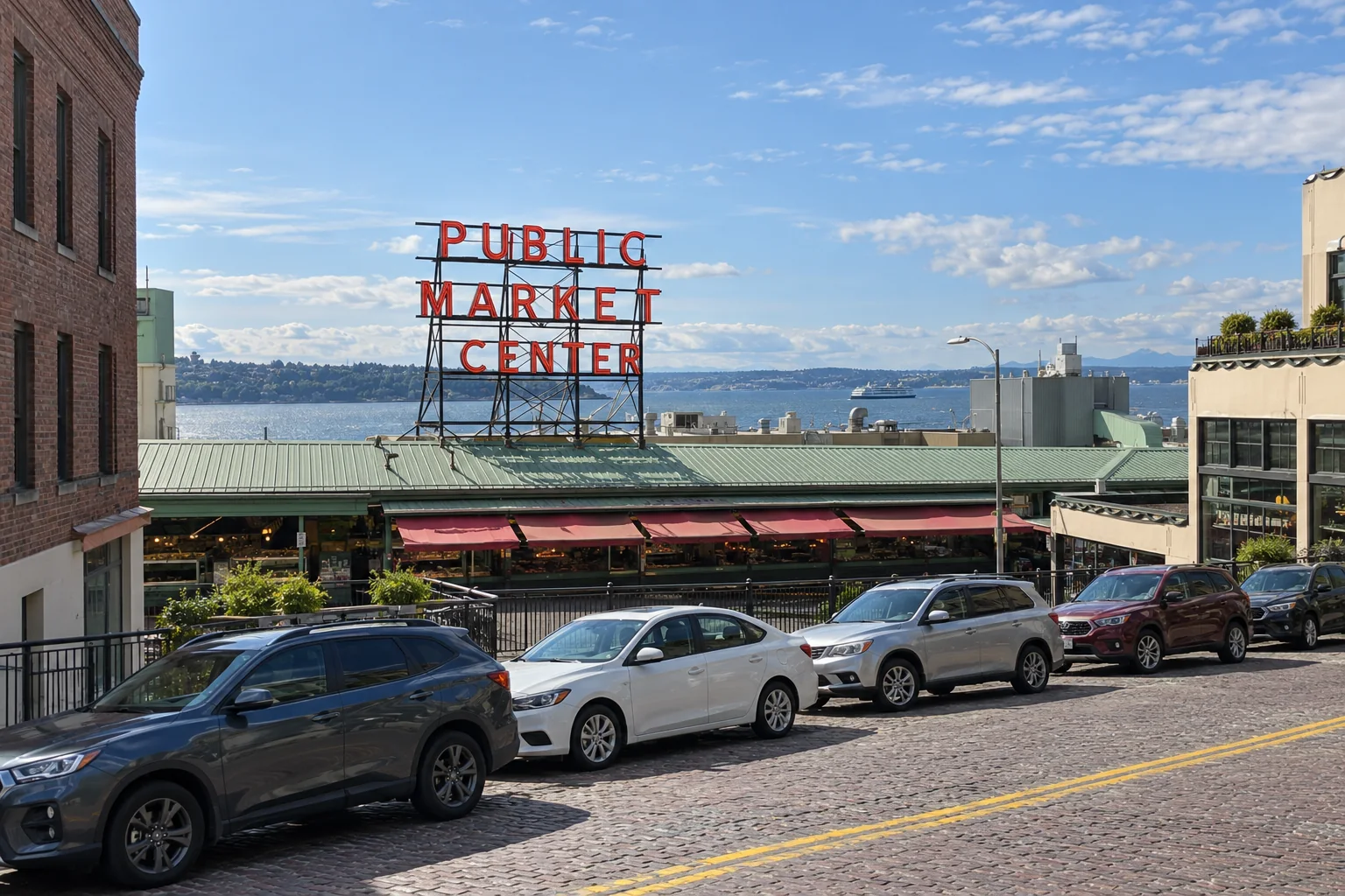 The market sign, green roof and red awnings of Pike Place Market from the street, with the harbour beyond.