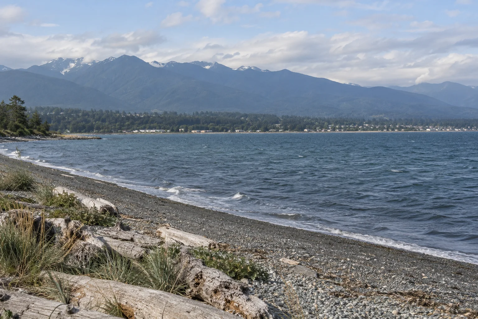 A pebble shore with driftwood on the Strait of Juan de Fuca at Port Angeles with the Olympic Mountains behind the town.