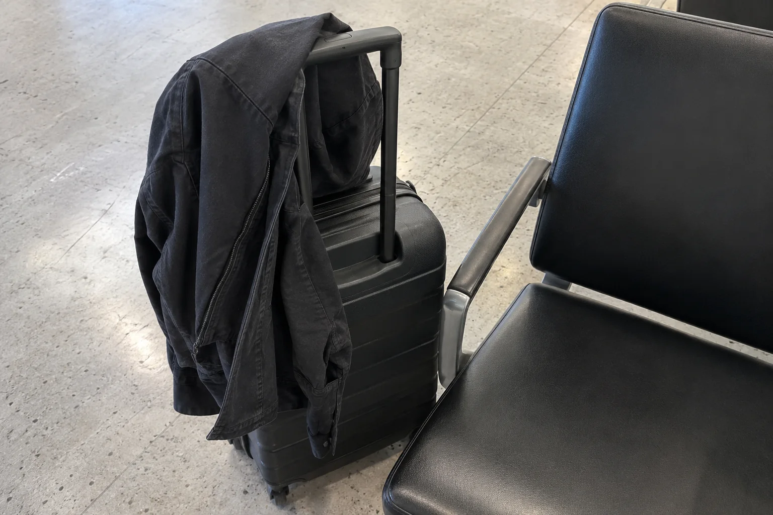 A dark jacket folded over a carry-on suitcase beside a black gate seat in the S Concourse at Seattle-Tacoma airport.