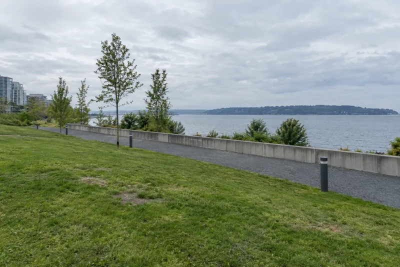 The lawn, gravel path and concrete wall of the Olympic Sculpture Park in Seattle above the bay.