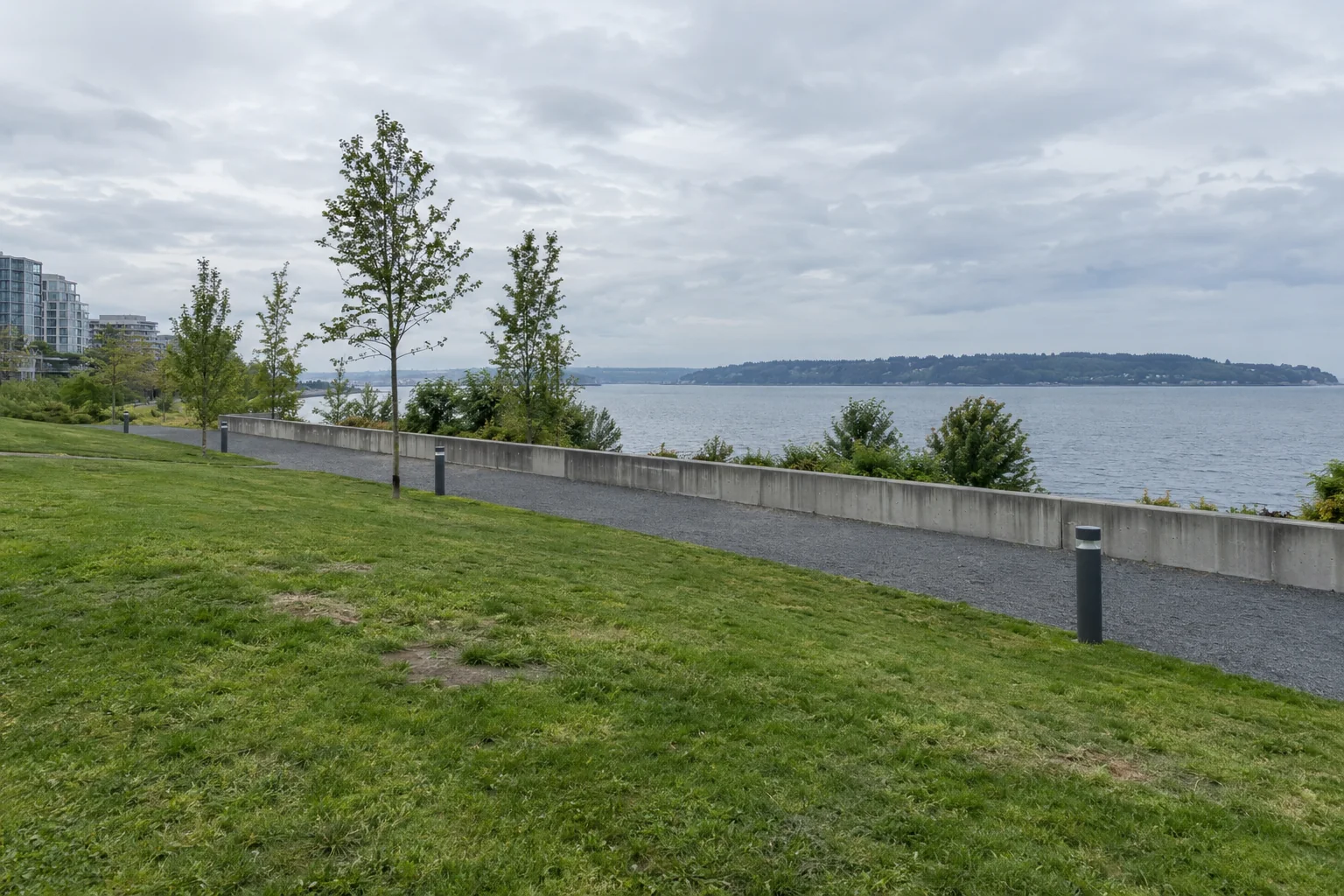 The lawn, gravel path and concrete wall of the Olympic Sculpture Park in Seattle above the bay.