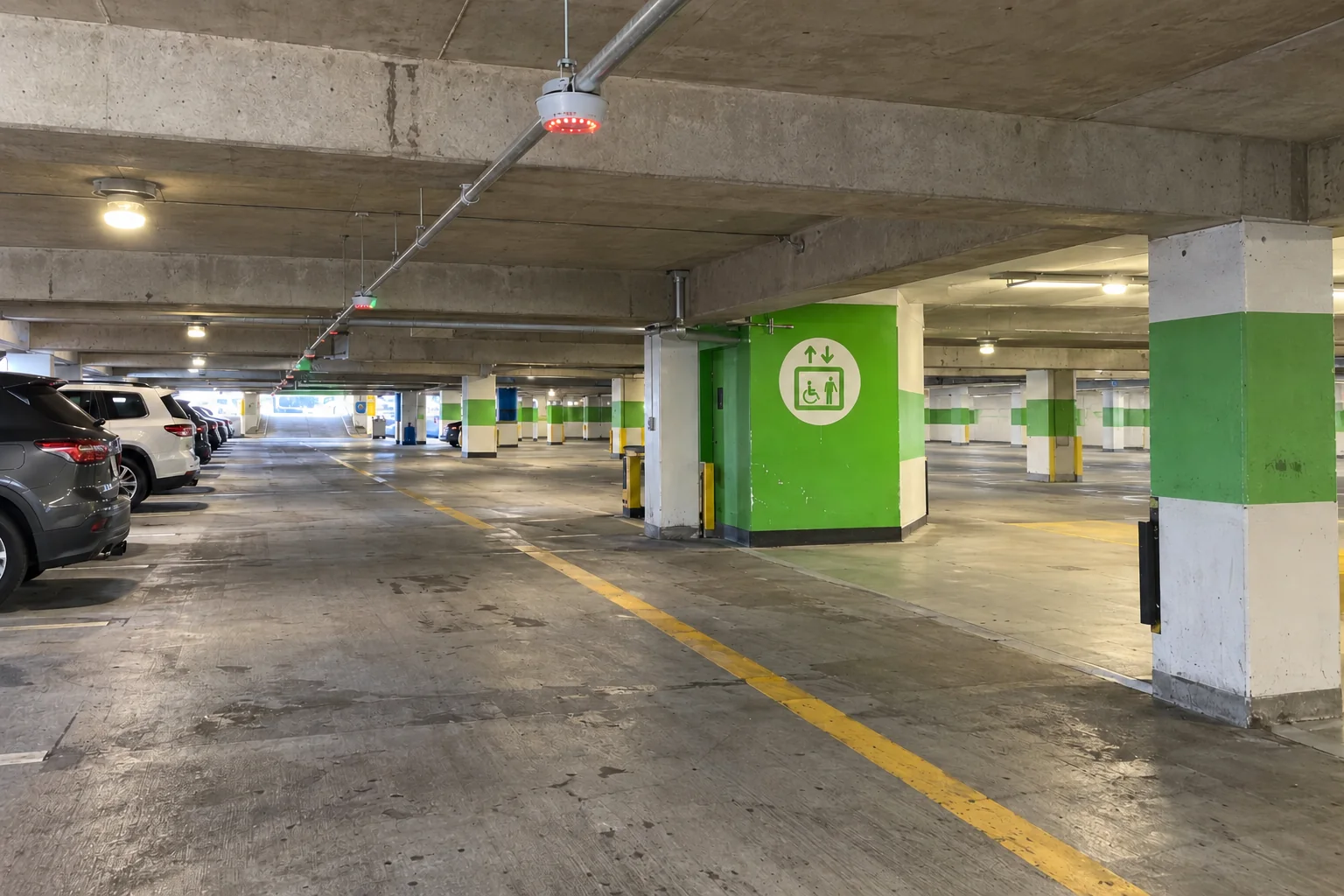 A covered level of the Seattle-Tacoma airport parking garage, with parked cars and a bright green elevator core