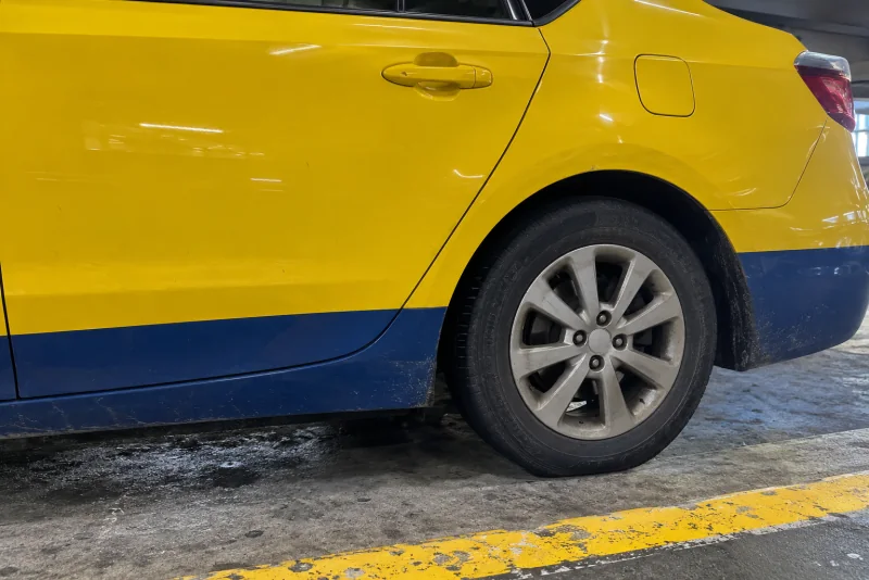 The yellow rear door and wheel of a taxi at the curb in the Seattle-Tacoma airport garage.