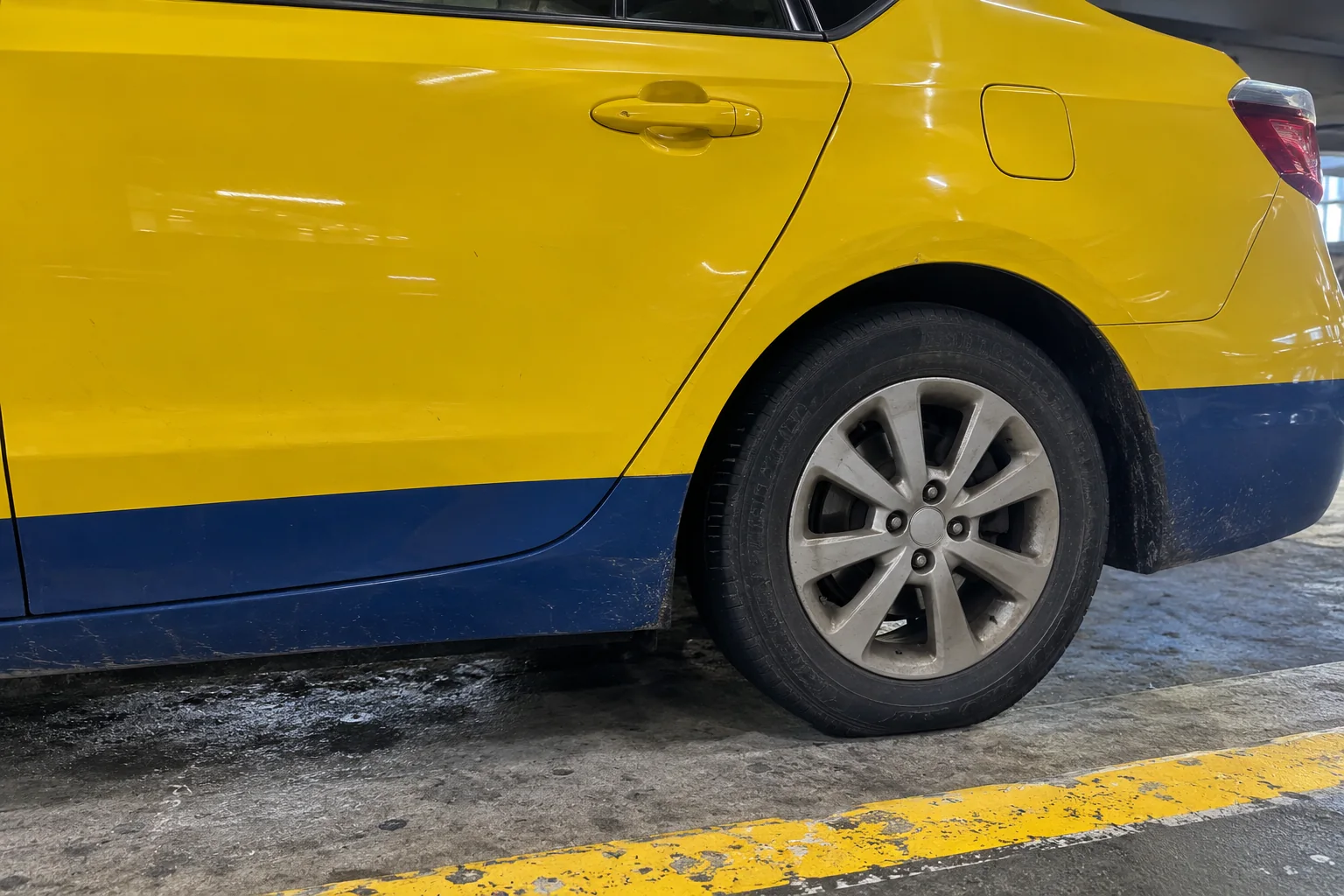 The yellow rear door and wheel of a taxi at the curb in the Seattle-Tacoma airport garage.