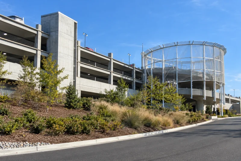 The curved wire-mesh ramp tower and grey concrete garage of the Rental Car Facility beside the road near Seattle-Tacoma airport.